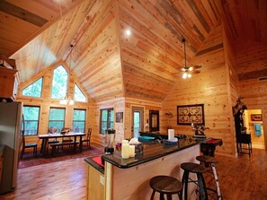 Una cabaña de madera espaciosa con un amplio comedor, una cocina con barra y una sala de estar acogedora.