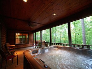 Una cabaña de madera con jacuzzi, terraza de madera y grandes ventanales con vista a un bosque.