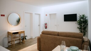 Una sala moderna con un sofá, un escritorio y una silla, un espejo redondo, un televisor de pantalla plana y una mesa de comedor con platos y vasos.