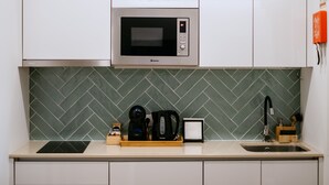 Una cocina con armarios blancos, microondas, hervidor de agua, cafetera y fregadero.