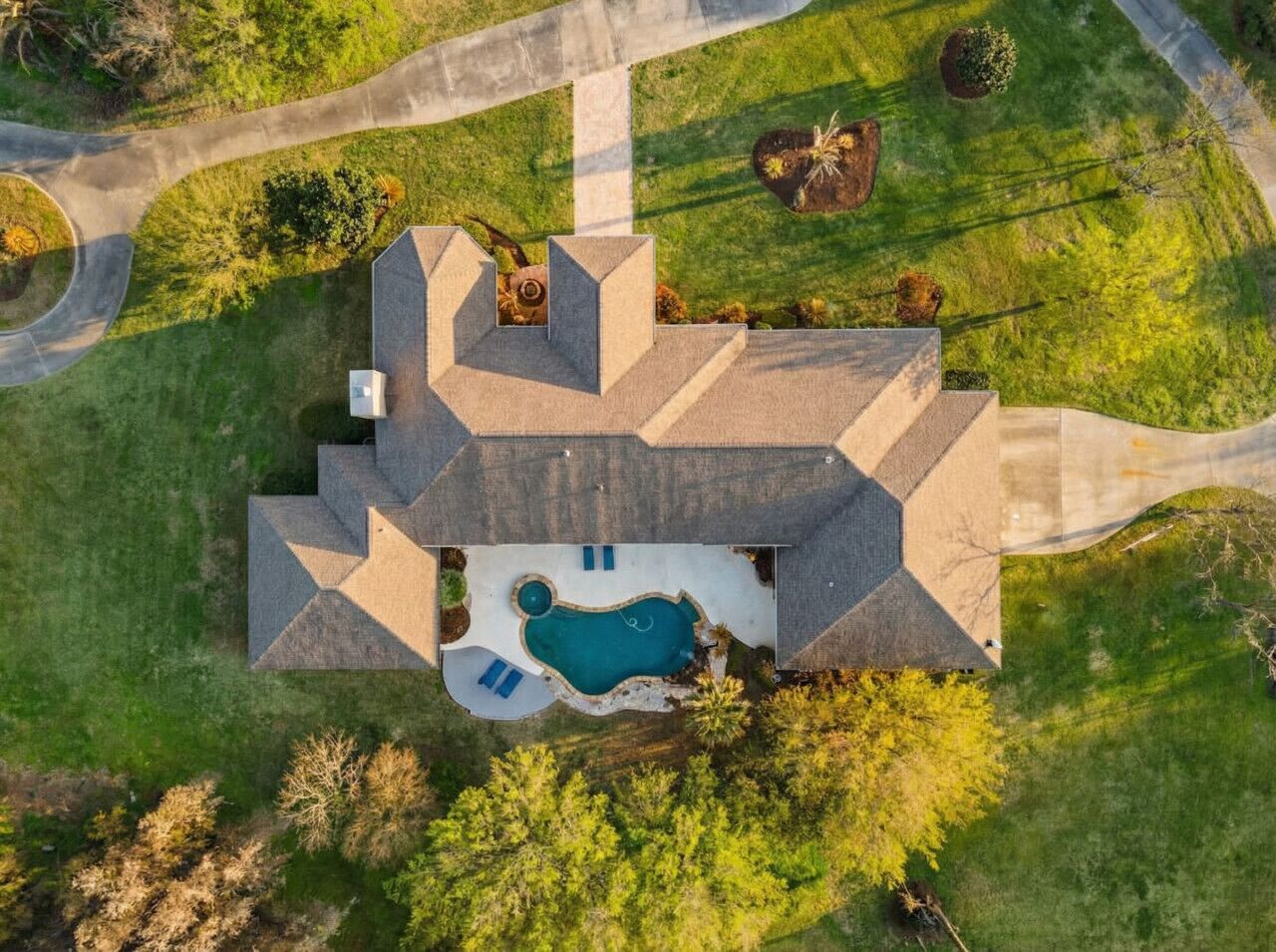 An aerial view of a house with a swimming pool, surrounded by a well-maintained lawn and trees.