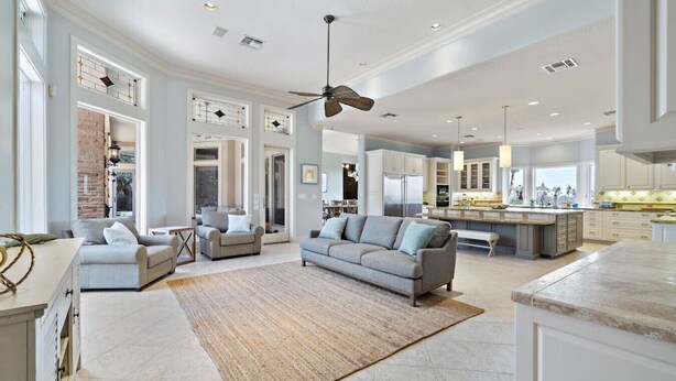 A spacious living room with a large sofa, a coffee table, and a rug. There is a kitchen area with a bar and a dining area with a table and chairs. - Luxurious Secluded Estate with Pool & Pond (Galveston)