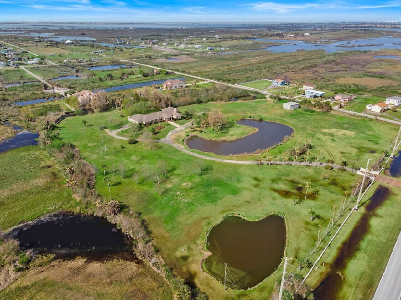 An aerial view of a rural area with multiple ponds, a large heart-shaped pond, and scattered houses.