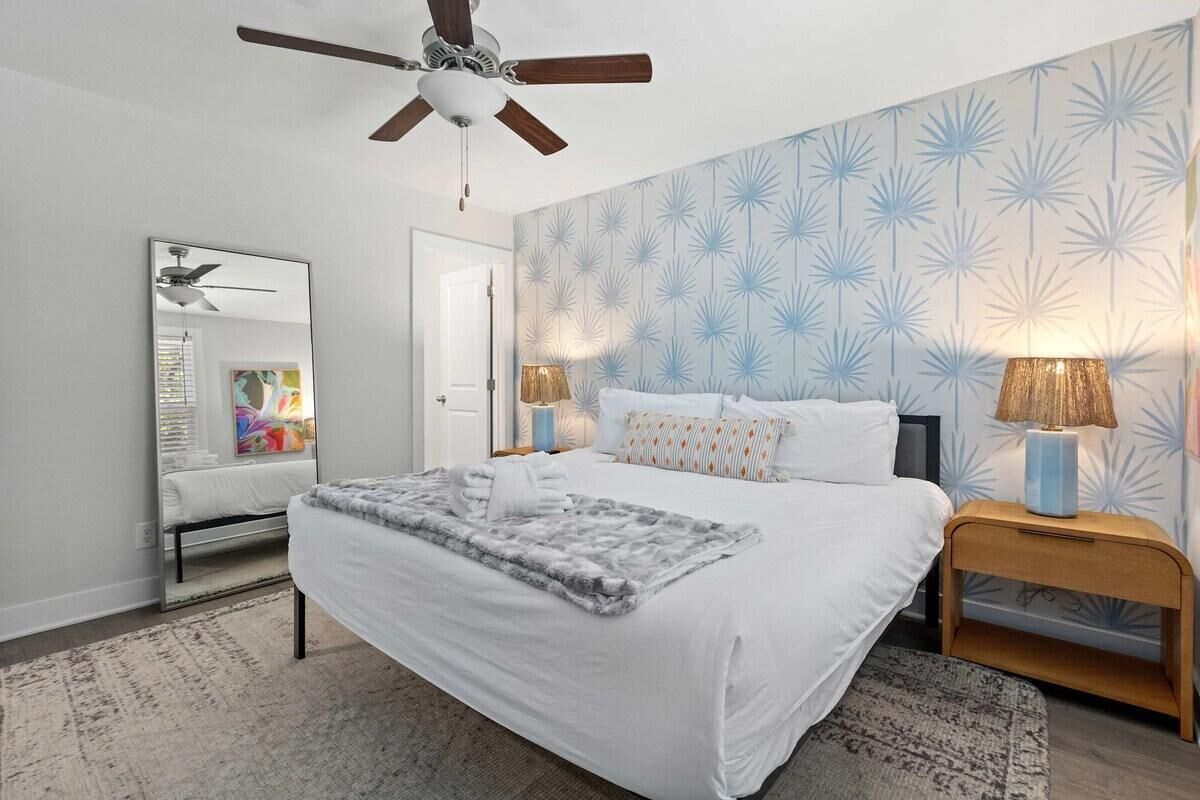 A bedroom with a bed, two bedside tables, a ceiling fan, a mirror, and a patterned wall.
