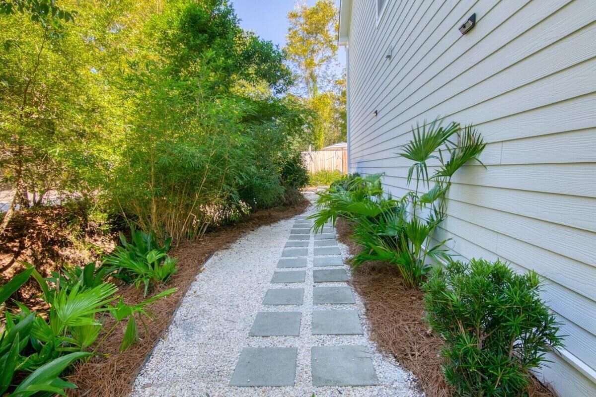 Un chemin menant à une maison à l’extérieur blanc, entourée de différentes plantes et arbres.