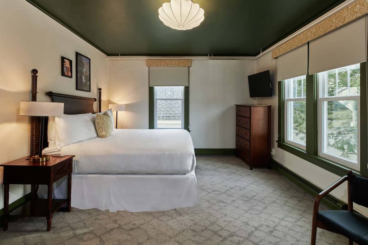 A bedroom with a bed, bedside tables, a dresser, a television, and large windows.