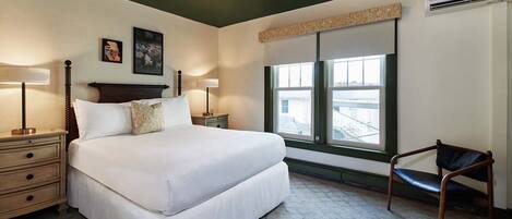 A bedroom with a large bed, two bedside tables, a chair, a window with a view, and a ceiling light fixture.