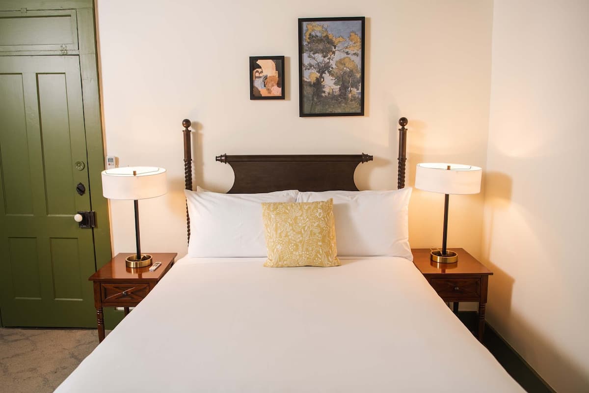 A neatly made bed with two bedside tables, each with a lamp, a green door, and two framed pictures on the wall.