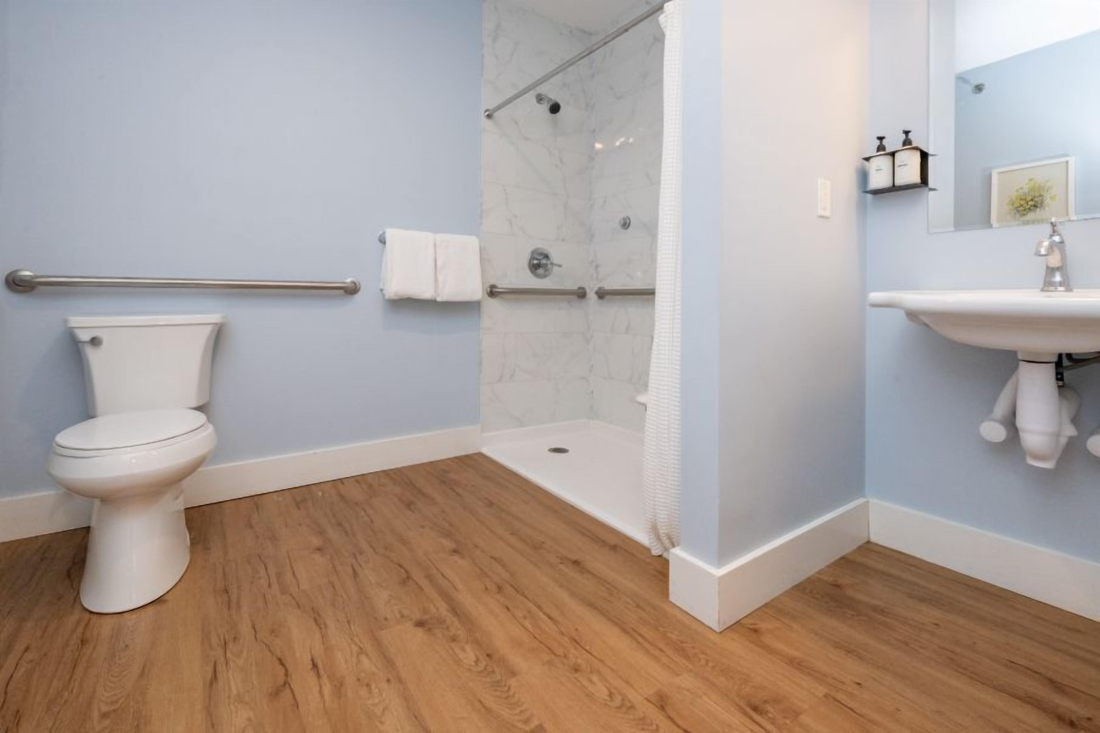 A bathroom with a toilet, a shower with a glass door, a sink, and a wooden floor.