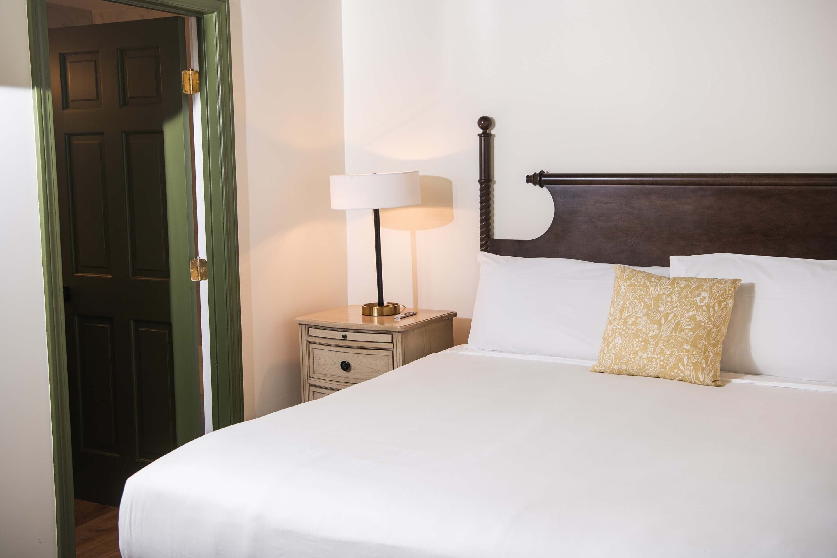 A neatly made bed with white linens, a bedside lamp, and a floral pillow.