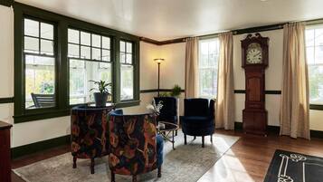 A room with a large window, a clock, a blue armchair, a patterned armchair, and a small table with a plant.