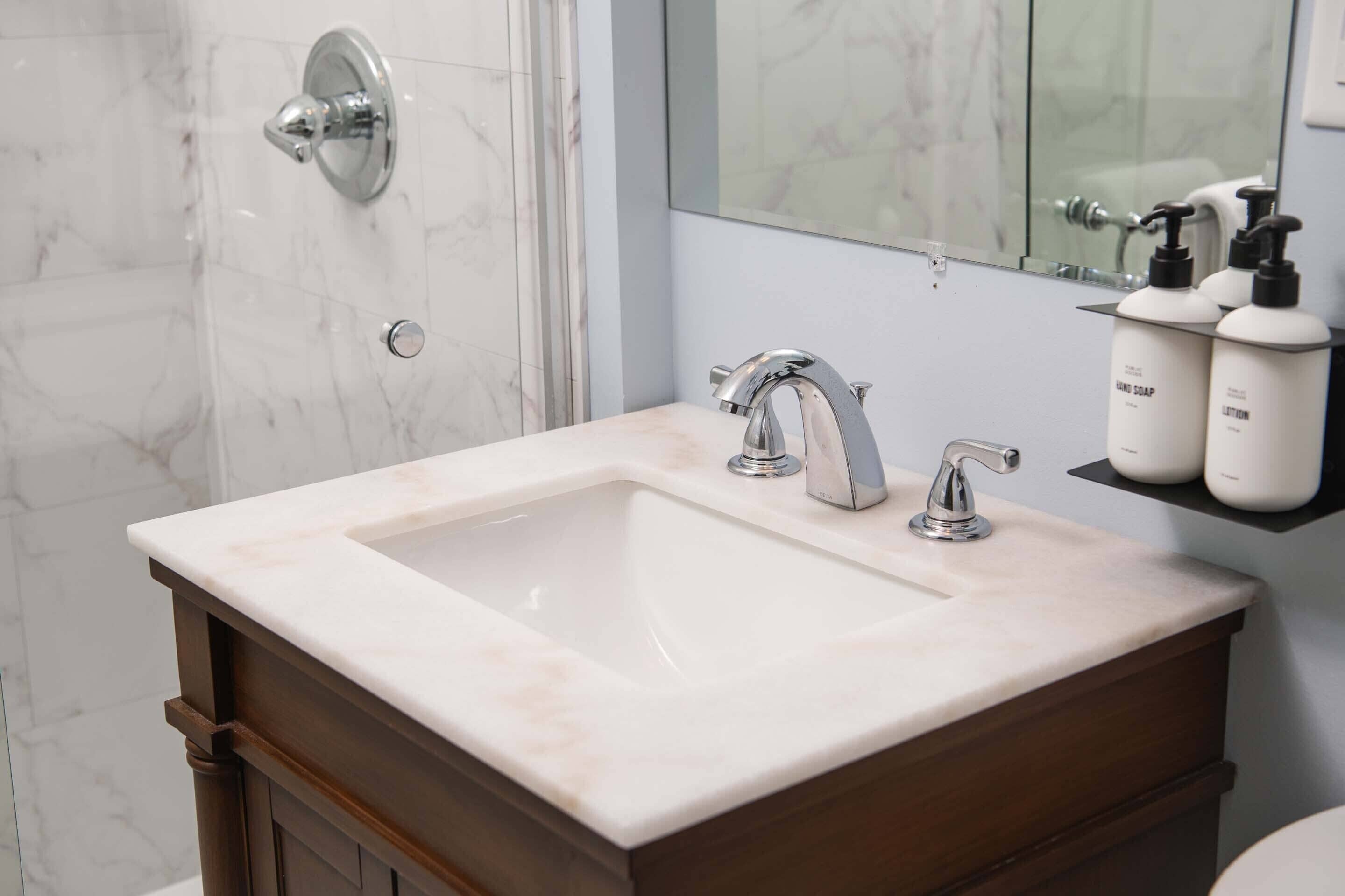A bathroom with a marble sink, a mirror, and a shower door.