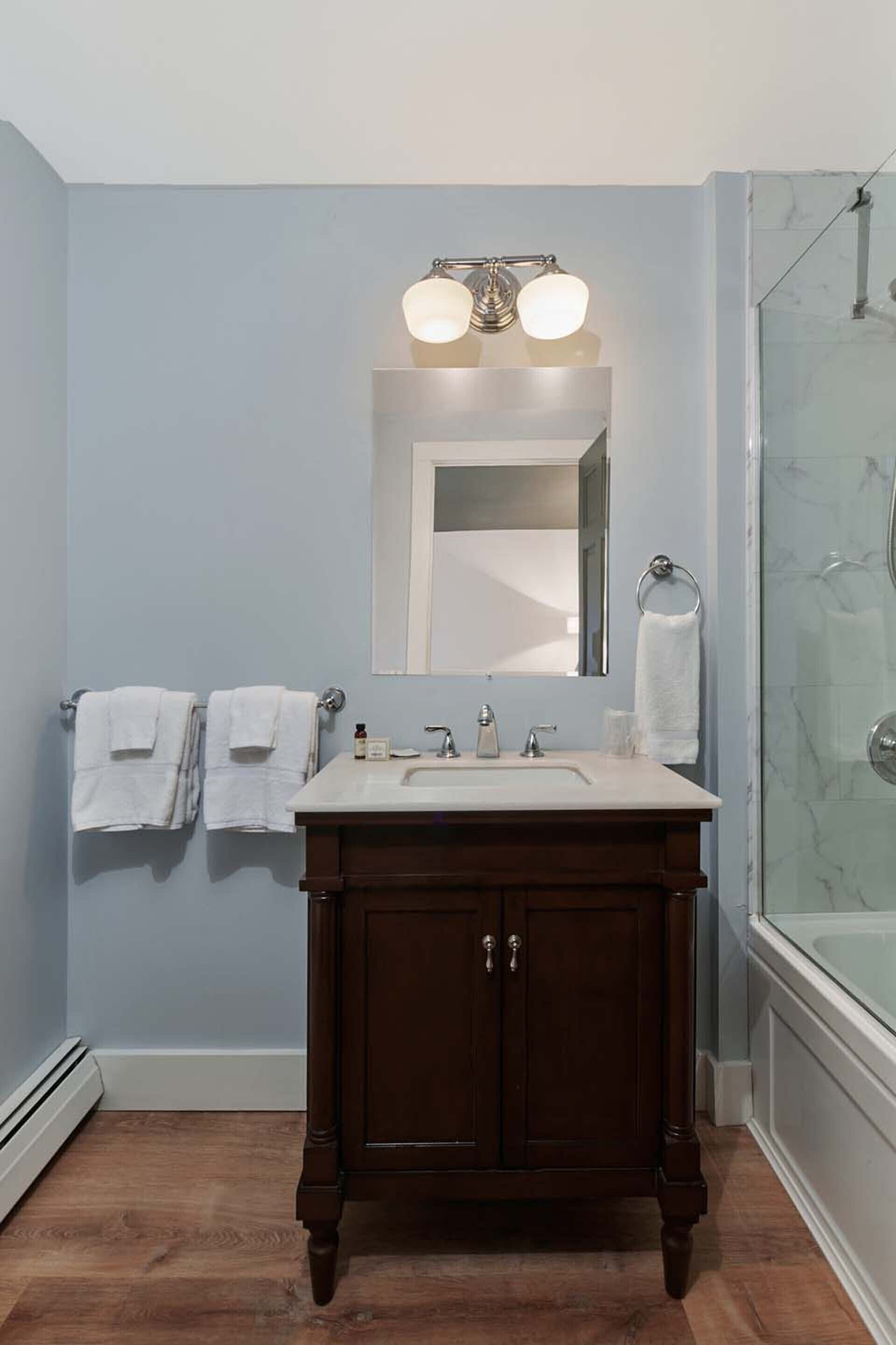 A bathroom with a wooden vanity, a white sink, a mirror, and a glass shower enclosure.