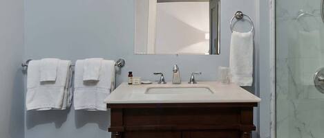 A bathroom with a wooden vanity, a white sink, a mirror, and a glass shower enclosure.