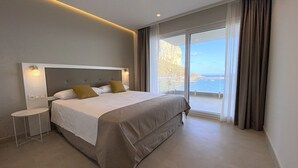 Moderni hotellihuone, jossa on suuri sänky, yöpöytä ja merinäköala, joka avautuu liukuovien kautta.