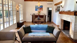 A spacious living room with a fireplace, wooden beams, a dining area, and large windows. - Villa for 8 people on the Gigaro beach (La Croix-Valmer)