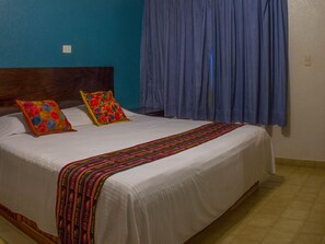 A bed with a white mattress, two colorful pillows, and a striped blanket.