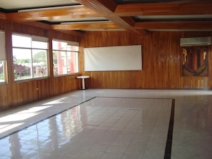 A spacious room with wooden paneling, large windows, a tiled floor, and a whiteboard on the wall.