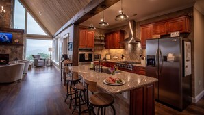 A spacious kitchen with wooden cabinets, a large island, stainless steel appliances, and a stone fireplace. - Luxury Lodge with Ride-In-Ride-Out Location - WiFi - Sweeping Mountain Views (Huntsville)