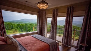 A bedroom with a large bed, a chandelier, and a balcony with a view of the mountains. - Luxury Lodge with Ride-In-Ride-Out Location - WiFi - Sweeping Mountain Views (Huntsville)
