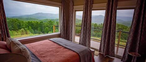 Une chambre avec un grand lit, un lustre et un balcon offrant une vue sur les montagnes.