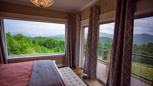 A bedroom with a large bed, a bench, and a view of a lush green landscape through large windows. - Luxury Lodge with Ride-In-Ride-Out Location - WiFi - Sweeping Mountain Views (Huntsville)