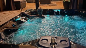 Ein Whirlpool mit blauer Beleuchtung, eine Holzterrasse und eine gemütliche Sitzecke mit Kissen und einem Blumentopf.