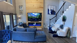 Ein modernes Wohnzimmer mit einem Ecksofa, einem Flachbildfernseher, einem Kamin und einer Treppe.