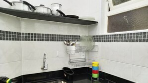 A kitchen with a black countertop, stainless steel sink, and a gas stove. There are pots and pans on the countertop, and a dish rack with utensils. - TC308 Aconchegante Studio na Praia (Rio de Janeiro)