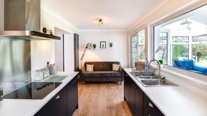 A modern kitchen with a central island, built-in oven, and stainless steel appliances. - Just Stay Wales - Hadland House Mumbles (Swansea)