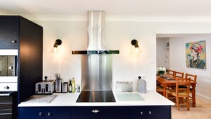 A modern kitchen with a stainless steel range hood, a built-in toaster, and a dining area with wooden chairs and a table. - Just Stay Wales - Hadland House Mumbles (Swansea)