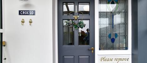 A dark blue door with a heart-shaped glass design, a 'Please remove your shoes' sign, and a 'CROESO' sign above the door.