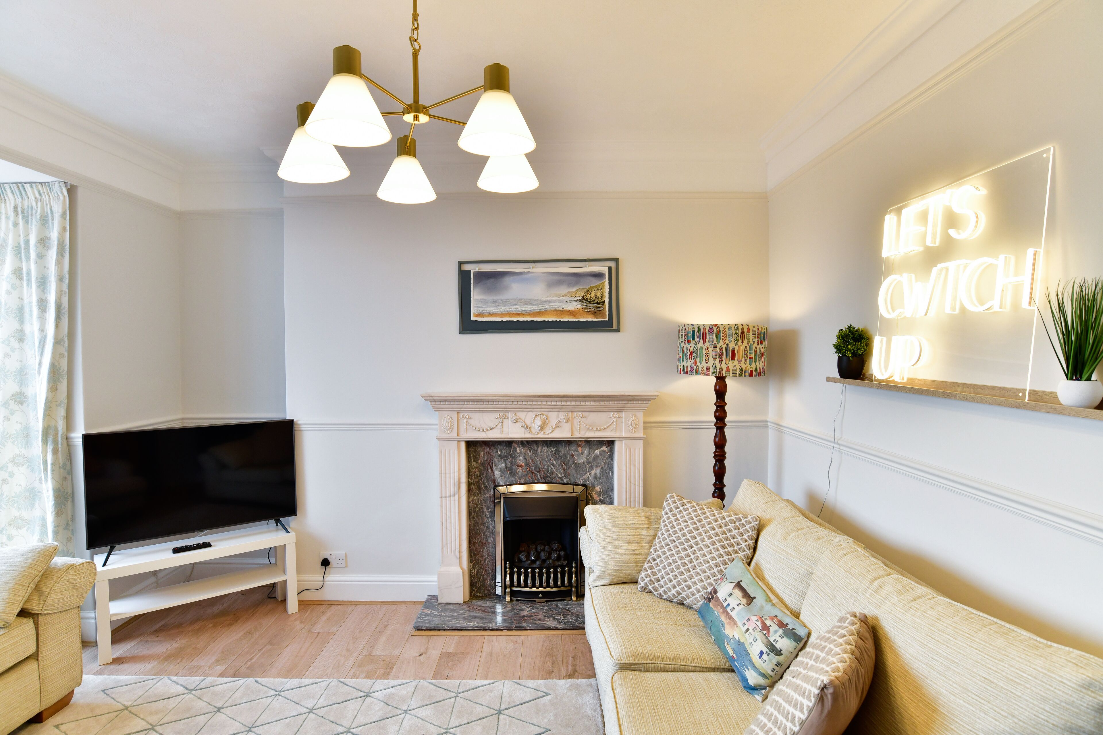 A living room with a flat-screen TV, a fireplace, a sofa, and a 'LET'S SWITCH UP' sign.