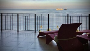 A balcony with a view of the sea, a chair, and a table.