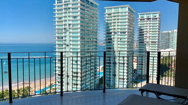 A balcony with a view of tall buildings, a beach, and the ocean.
