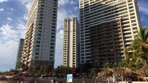 A beachfront hotel with multiple high-rise buildings, palm trees, and beach umbrellas.