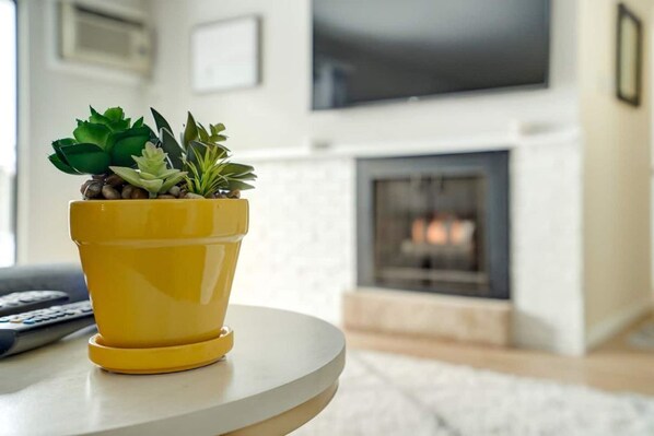 A yellow pot with succulents on a white table in a living room with a fireplace in the background.