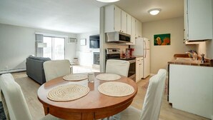 Una cocina moderna con armarios blancos, un microondas y un refrigerador. Hay una mesa de comedor con cuatro sillas y una alfombra.