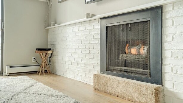 Una sala moderna con chimenea de ladrillo blanco, un calentador portátil y un televisor montado en la pared.