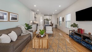 A modern living room with a sofa, coffee table, and TV. - Modern Townhouse: 3-Bed Haven, Vibrant Pink Door! (Nashville)