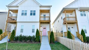 A two-story apartment building with a central entrance, wooden balconies, and a picket fence. - Modern Townhouse: 3-Bed Haven, Vibrant Pink Door! (Nashville)