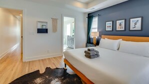 A hotel room with a bed, a nightstand, a mirror, a window with curtains, and a door leading to a bathroom. - Modern Townhouse: 3-Bed Haven, Vibrant Pink Door! (Nashville)