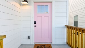 A pink door with a window, a wooden bench, a doormat, and a light fixture. - Modern Townhouse: 3-Bed Haven, Vibrant Pink Door! (Nashville)