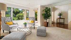 Un salon spacieux avec deux fauteuils gris, une table basse ronde et une grande plante en pot.