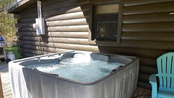 A hot tub in front of a log cabin with a window above it.