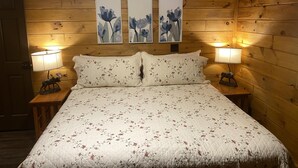 Una habitación con paneles de madera, una cama, dos lámparas de noche y tres cuadros florales colgados en la pared.
