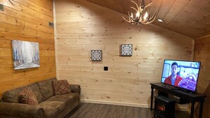 Una habitación acogedora con paredes de madera, un sofá de cuero marrón, una televisión y una chimenea.