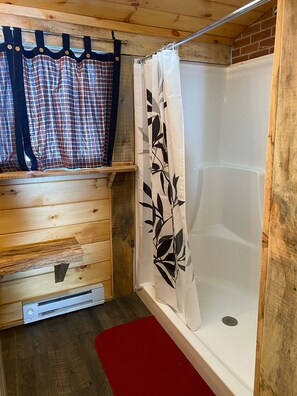 A wooden cabin bathroom with a shower, a red bath mat, and a wooden bench.