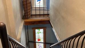 A wooden staircase with black railings leading to a landing with a large vase and a stained glass window depicting birds.