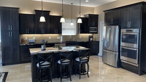 A modern kitchen with dark cabinetry, stainless steel appliances, and a central island with bar stools. - Waterfront Luxury House on the Bay -  North Ocean City (Ocean City)